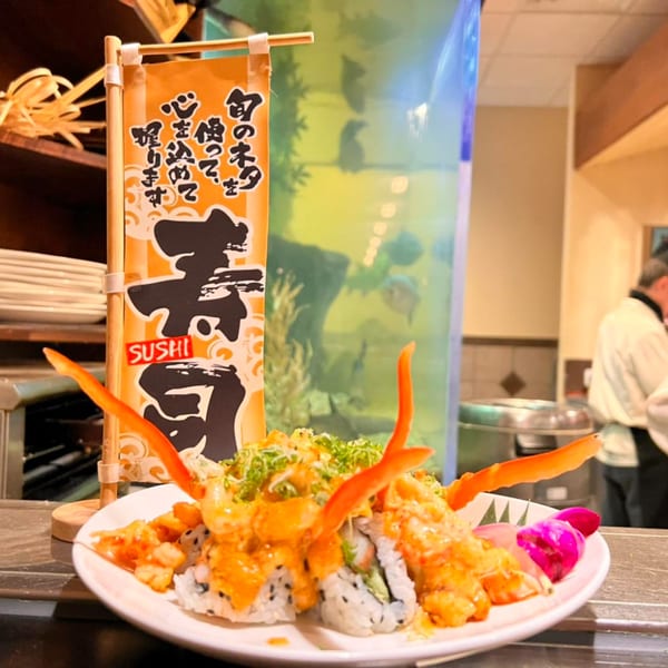 A plate of House of Hunan sushi rolls topped with crab legs and sauce, next to a sushi banner.