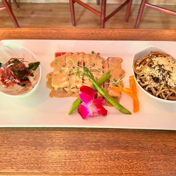 Seared tuna with sauce, asparagus, and an orchid, served with two side dishes.
