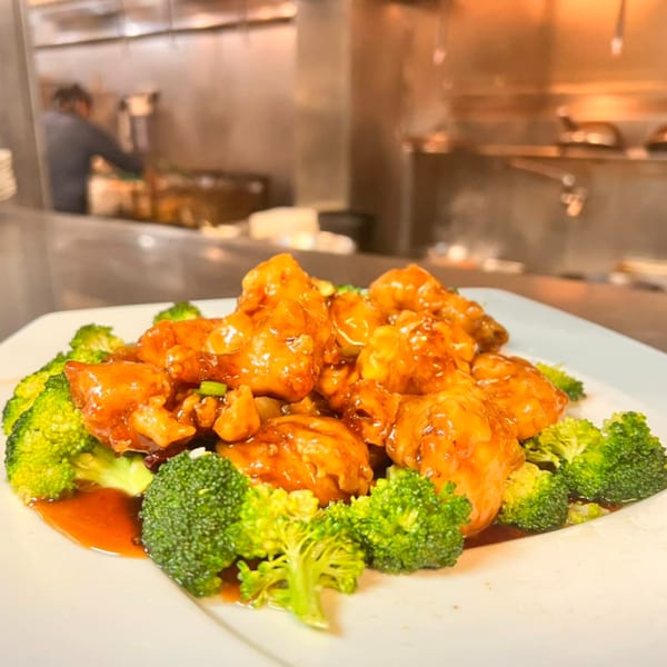 House of Hunan's General Tso's chicken with broccoli, served on a white plate with a chef in the background.