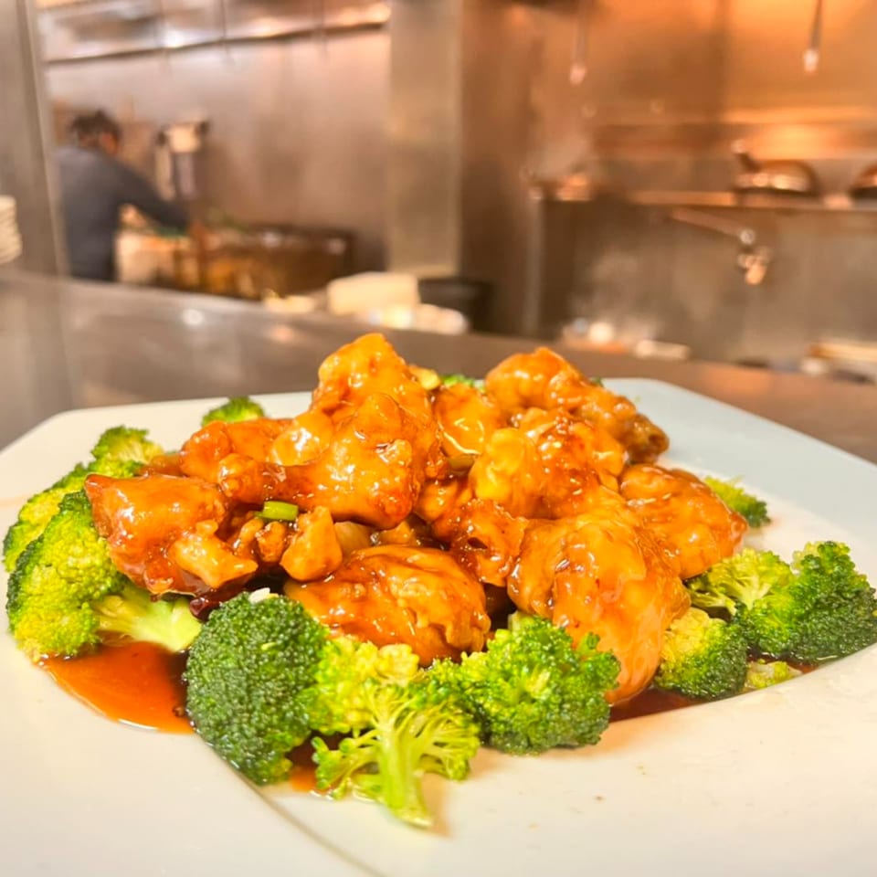 House of Hunan's General Tso's chicken with broccoli, served on a white plate with a chef in the background.