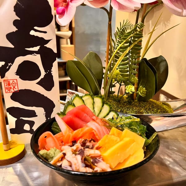 A colorful poke bowl with tuna, salmon, cucumber, and mango, next to a decorative plant.