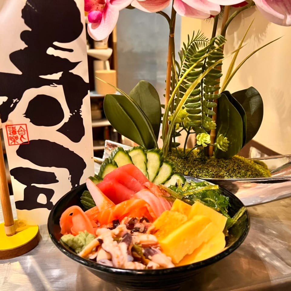 A colorful poke bowl with tuna, salmon, cucumber, and mango, next to a decorative plant.
