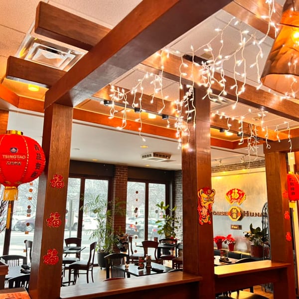 Interior of House of Hunan restaurant with wooden beams, festive lights, and red lanterns.